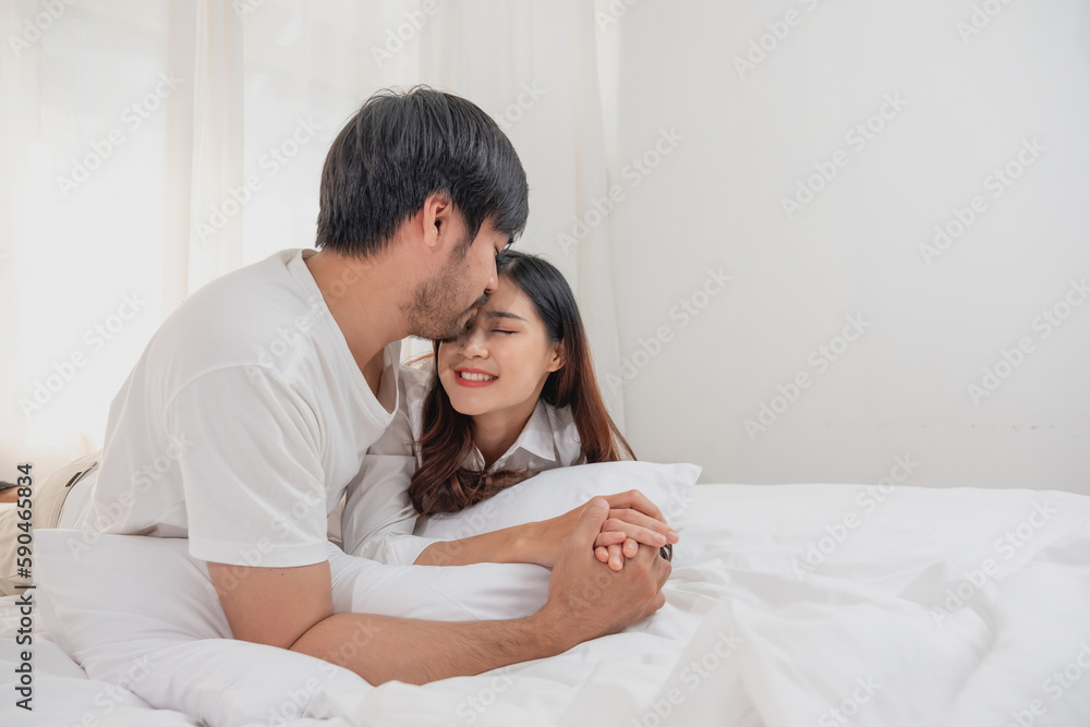 Fototapeta premium Happy young asian couple embracing, teasing, playing cheerfully in bed at home, romantic time to enhance family bonding. family concept.