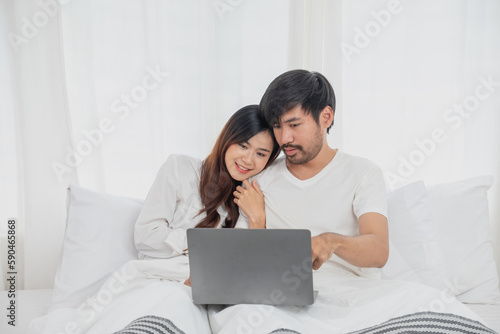 Young happy asian couple using laptop in bed watching movie, romantic time to enhance family relationship, family concept.