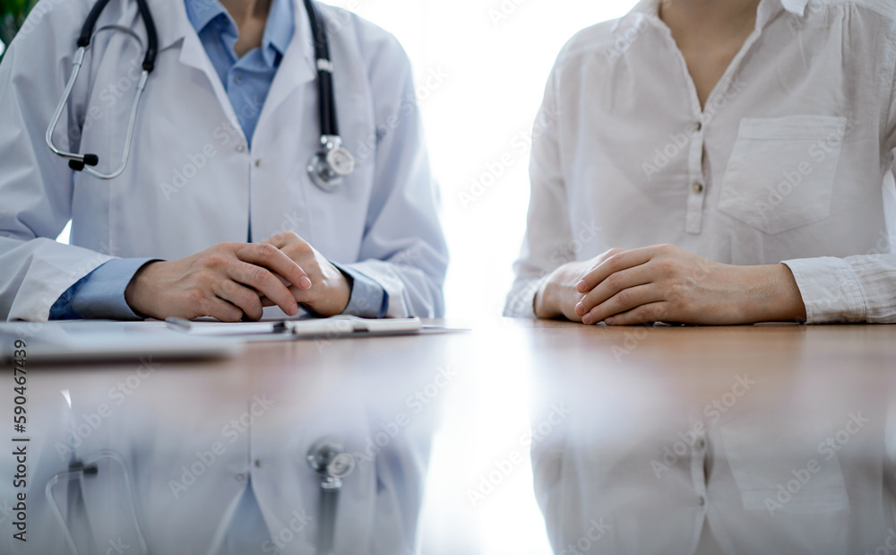 Doctor and patient discussing something while sitting near each other at the wooden desk in clinic. Medicine concept Doctor and patient discussing something while sitting near each other at the wooden desk in clinic. Medicine concept