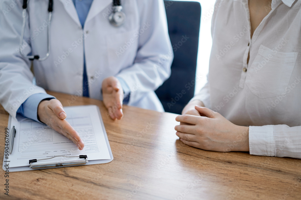 Doctor and patient discussing something while sitting near each other at the wooden desk in clinic, view from above. Medicine concept Doctor and patient discussing something while sitting near each other at the wooden desk in clinic, view from above. Medicine concept