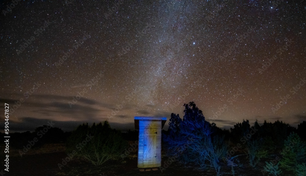 Wooden outdoor toilet in nature under a beautiful dark starry night sky