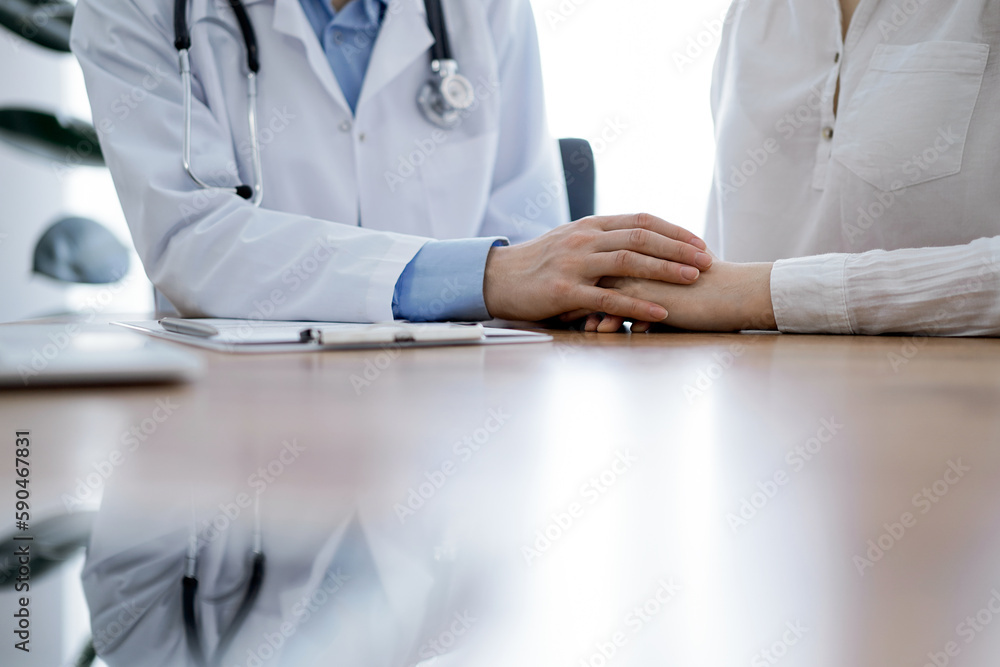 Doctor and patient sitting near each other at the wooden table in clinic. Female physician's hands reassuring woman. Medicine concept Doctor and patient sitting near each other at the wooden table in clinic. Female physician's hands reassuring woman. Medicine concept