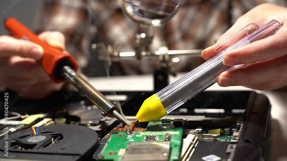 a man is soldering in a repair shop. repair of the board with a soldering iron a man is soldering in a repair shop. repair of the board with a soldering iron