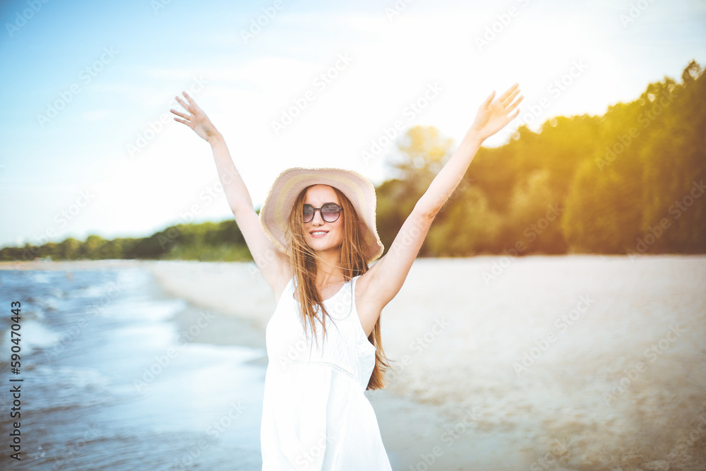 Happy smiling woman in free happiness bliss on ocean beach standing with a hat, sunglasses, and rasing hands. Portrait of a multicultural female model in white summer dress enjoying nature Happy smiling woman in free happiness bliss on ocean beach standing with a hat, sunglasses, and rasing hands. Portrait of a multicultural female model in white summer dress enjoying nature