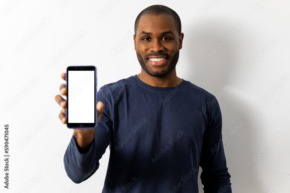 Satisfied smiling dark-skinned man showing white screen mobile phone to camera standing isolated on white space in studio. Concept of sales promotion, advertising, marketing.