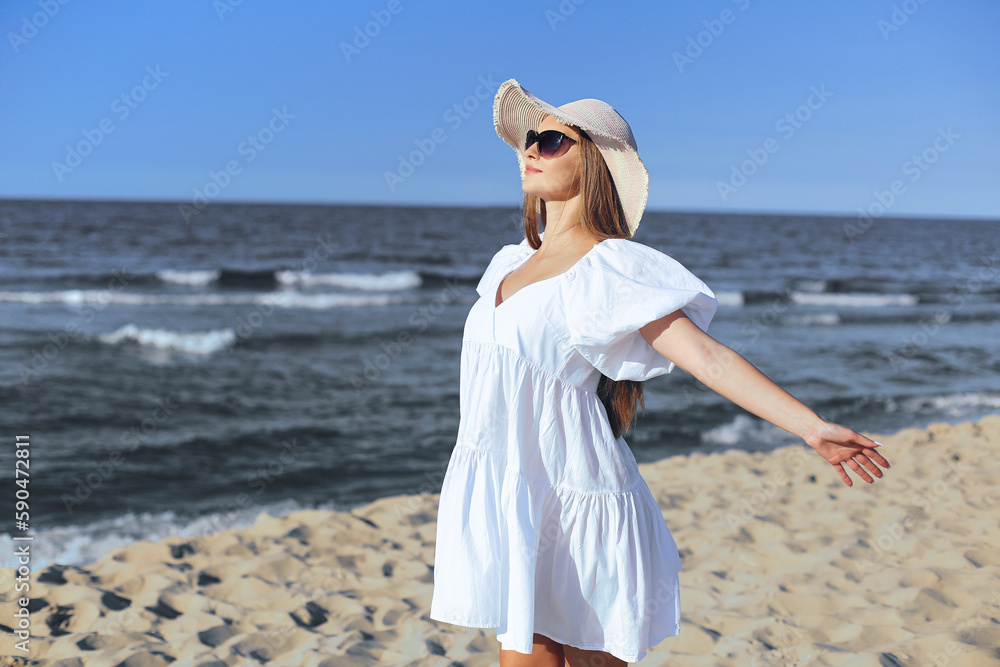 Happy blonde woman is on the ocean beach in a white dress and sunglasses, open arms Happy blonde woman is on the ocean beach in a white dress and sunglasses, open arms