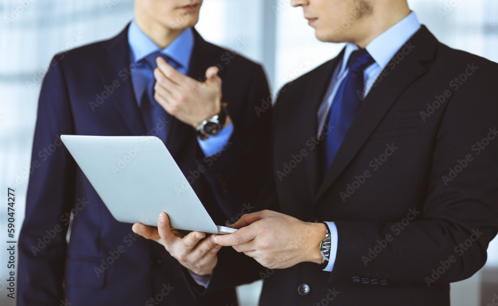Business people discussing a presentation at meeting, standing in a modern office. Unknown businessman with a colleague search for some information at the laptop, lawyers at negotiation Business people discussing a presentation at meeting, standing in a modern office. Unknown businessman with a colleague search for some information at the laptop, lawyers at negotiation