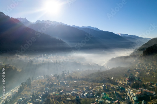 aerial drone shot gaining height over fog covered valley town of manali hill station with himalaya range in distance showing this popular tourist destination