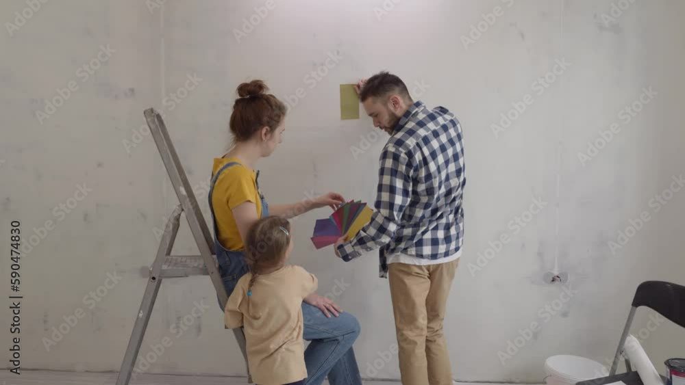 Cheerful parents with their daughter looking at color samples at home choosing paint for wall during apartment redecoration and construction. Renovation and improvement home for family. slow motion Cheerful parents with their daughter looking at color samples at home choosing paint for wall during apartment redecoration and construction. Renovation and improvement home for family. slow motion