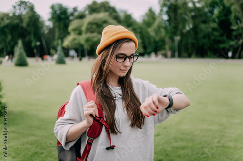 stylish young woman in Casual looks in Smart Watch on the background of a city park