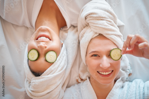 Friends, face and teenager, girl and facial, pampering and beauty, cucumber in portrait for skincare treatment. Happiness, people have fun together and female friendship, cosmetic care and top view photo