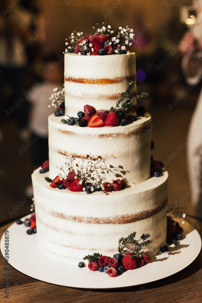 Cake in three tiers for the newlyweds. Beautiful white three-tiered wedding cake decorated with natural berries: raspberries, blueberries and strawberries.Wedding cake with berry decoration.