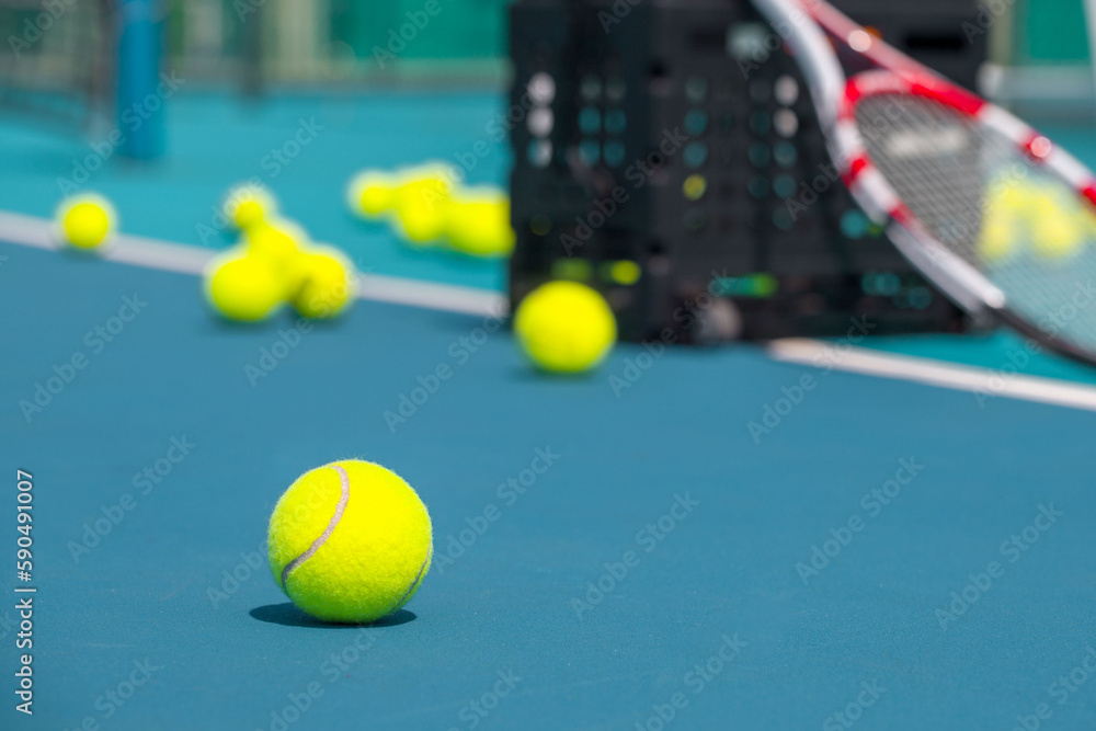 Tennis racket, balls and basket for tennis balls on hard blue court