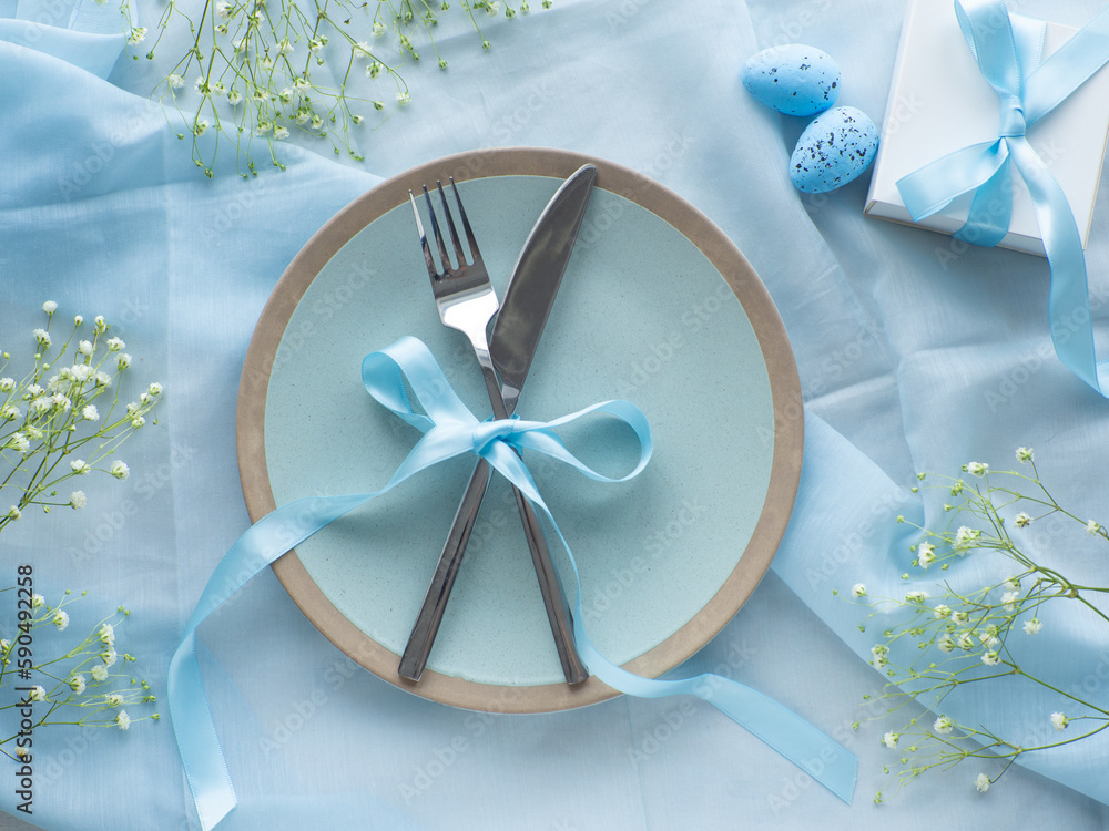 Festive Easter table setting with flowers, painted eggs and gift box on blue background flat lay. Elegance pastel and blue tablescapes. Easter celebration. Delicate Easter composition. View from above