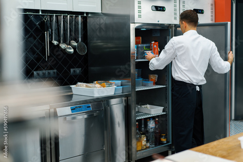 professional kitchen chef looks into the fridge and chooses ingredients for cooking food concept