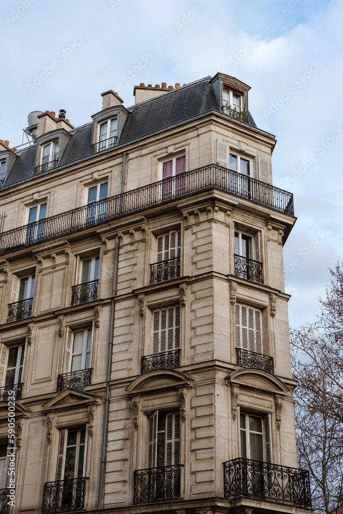 Obraz premium Exterior of aged residential building of beige color with glass windows and beautiful cast iron balconies located in the center of Paris, France