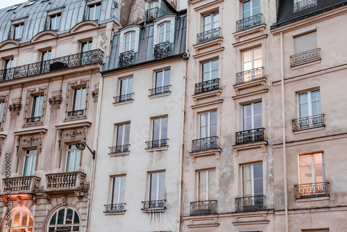 Exterior of aged residential building of beige color with glass windows and beautiful cast iron balconies located in the center of Paris, France