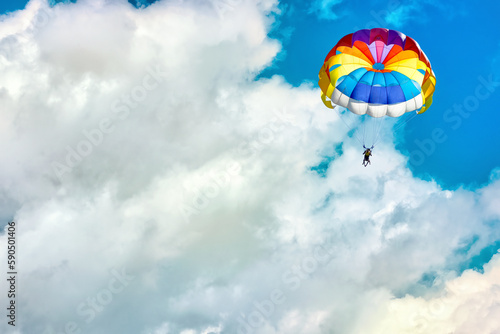 Paragliding using a parachute on background of blue cloudy sky.