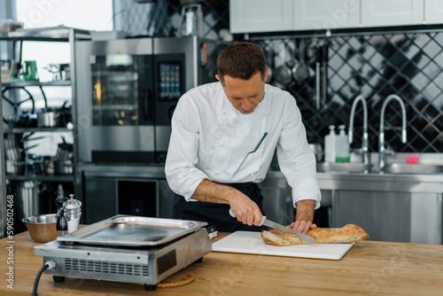 Professional modern kitchen in restaurant chef cuts fresh baked ready bread from oven for toast with knife