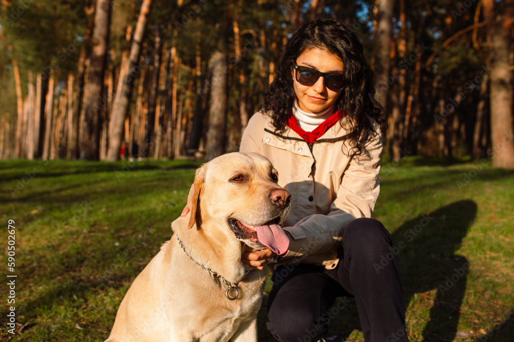 A stunning young woman accompanied by her Labrador Retriever in the forest during the spring season, caught in the act of a sunset stroll. A stunning young woman accompanied by her Labrador Retriever in the forest during the spring season, caught in the act of a sunset stroll.