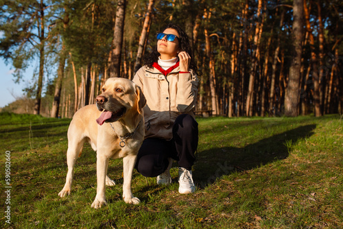A beautiful girl with her labrador in the spring forest. Young attarective woman in a denim suit with a dog at sunset. Labrador Retriever.