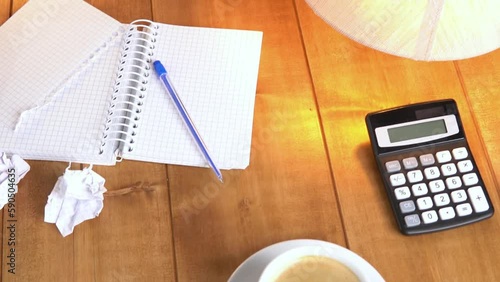 Coffee and a notebook on a brown wooden table under table lamp with warm light, slow motion video.