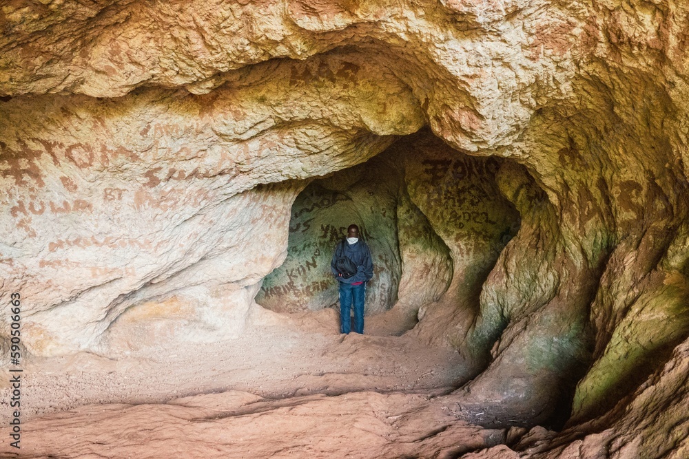 Obraz premium Rear view of a hiker in a cave against the background of Sipi Waterfall in Mount Elgon, Mbale, Uganda