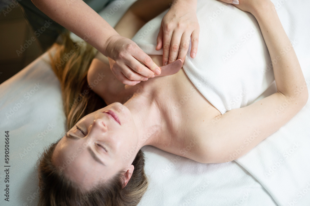 Hands of the masseur are close-up using a metal massage tool to massage the body of a woman lying on a couch. Health concept, body care, skin care, wellness Hands of the masseur are close-up using a metal massage tool to massage the body of a woman lying on a couch. Health concept, body care, skin care, wellness