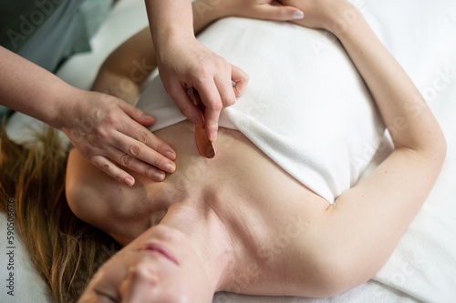 Hands of the masseur are close-up using a metal massage tool to massage the body of a woman lying on a couch. Health concept  body care  skin care  wellness