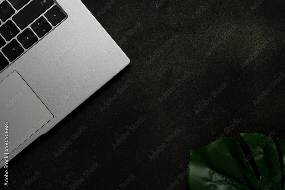 Workspace with laptop and palm leaves on black background. Flat lay