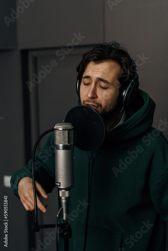 Rap singer with headphones and microphone emotionally recording new song in professional recording studio