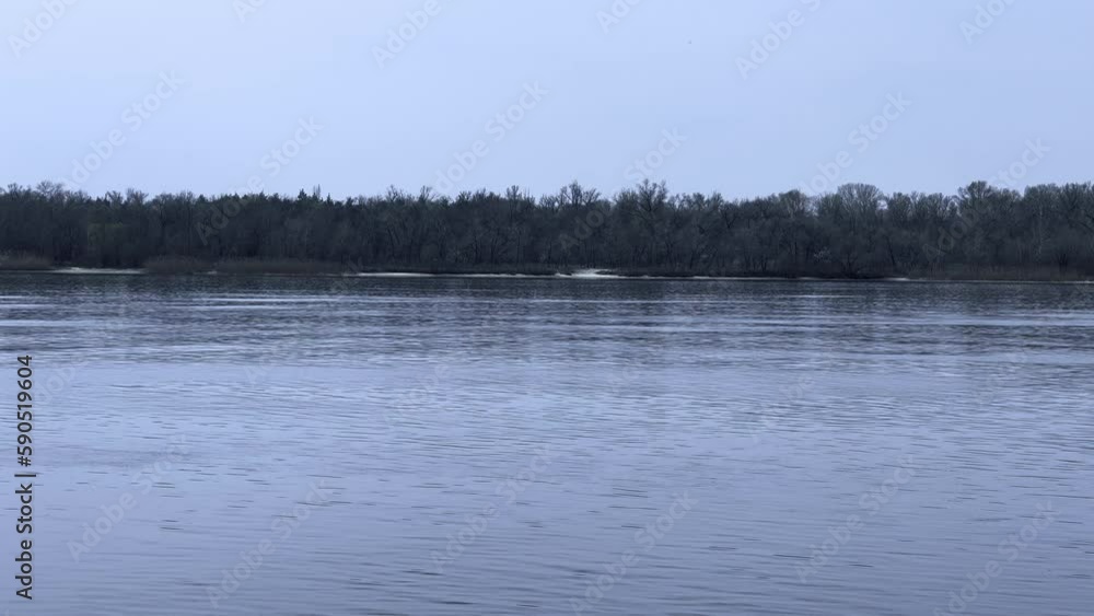 A quiet river with calm flow on a cloudy day, trees without leaves on the opposite bank. A quiet river with calm flow on a cloudy day, trees without leaves on the opposite bank.