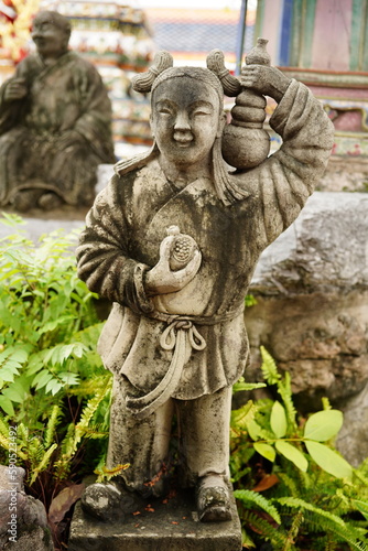 Ancient sandstone sculptures dressed like Chinese people in various poses at Wat Pho, Bangkok, Thailand.