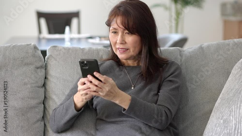 Attractive stylish woman texting reading messages on mobile cell phone sitting on sofa