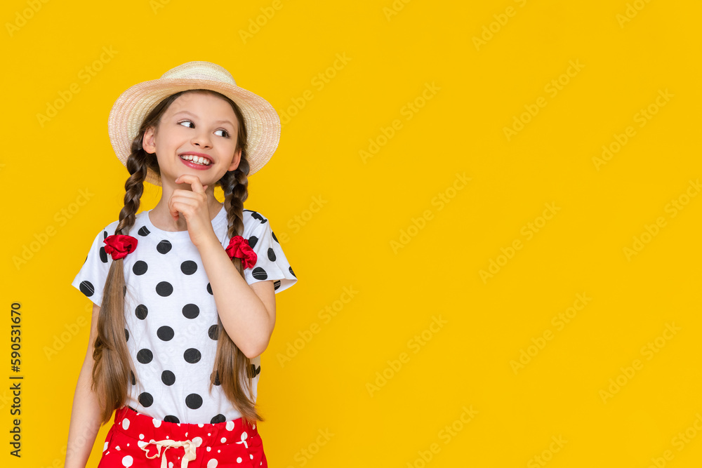 A beautiful little girl in polka dot shorts and a straw hat looks at your advertisement. Summer holidays. A teenage girl is waiting for summer on a yellow isolated background. Copy Space A beautiful little girl in polka dot shorts and a straw hat looks at your advertisement. Summer holidays. A teenage girl is waiting for summer on a yellow isolated background. Copy Space
