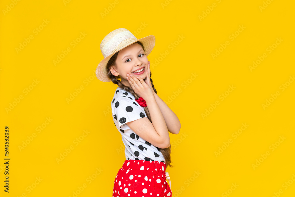 A charming little girl in a straw hat. A beautiful child rejoices in the summer and holds his cheeks with his hands. Cute teenage girl on a yellow isolated background. A charming little girl in a straw hat. A beautiful child rejoices in the summer and holds his cheeks with his hands. Cute teenage girl on a yellow isolated background.