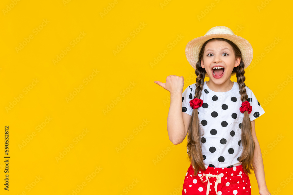 A beautiful little girl in polka dot shorts and a straw hat is pointing at your advertisement. Summer holidays. A teenage girl is waiting for summer on a yellow isolated background. Copy Space A beautiful little girl in polka dot shorts and a straw hat is pointing at your advertisement. Summer holidays. A teenage girl is waiting for summer on a yellow isolated background. Copy Space