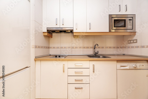 Frontal image of a kitchen with white cabinets with gray metal handles, wooden details and a matching countertop