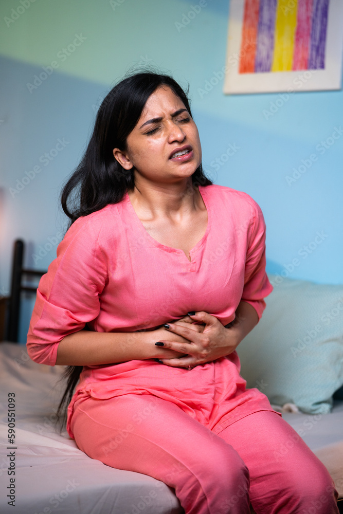 Vertical shot of girl suffering from stomach pain during late night at home - concept of menstruation cycle, health problems and unwell Vertical shot of girl suffering from stomach pain during late night at home - concept of menstruation cycle, health problems and unwell