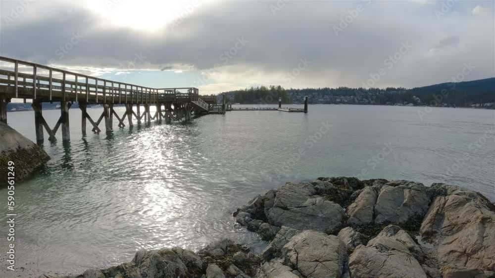 Wooden Quay on a rocky beach in Indian Arm, Vancouver, British Columbia, Canada. Belcarra Pier, West Coast of Pacific Ocean. Spring Season Sunny Cloudy Evening. Slow Motion Wooden Quay on a rocky beach in Indian Arm, Vancouver, British Columbia, Canada. Belcarra Pier, West Coast of Pacific Ocean. Spring Season Sunny Cloudy Evening. Slow Motion