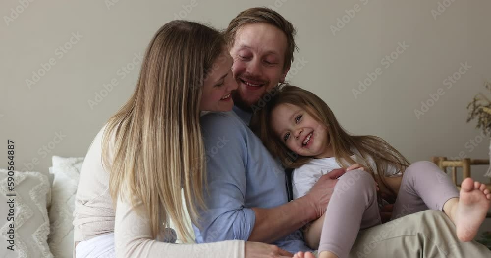 Happy parents tickling sweet little daughter kid on couch, bed, holding child on lap, playing active game together, laughing, enjoying family playtime, leisure, parenthood Happy parents tickling sweet little daughter kid on couch, bed, holding child on lap, playing active game together, laughing, enjoying family playtime, leisure, parenthood