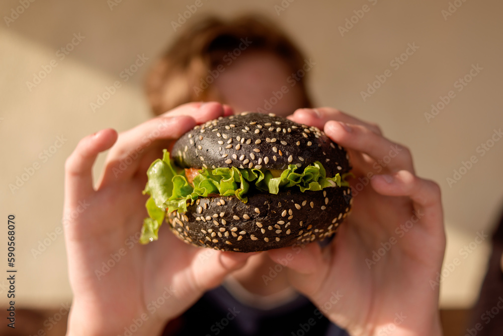Yummy homemade burgers in hand. Sesame bun, green salad, pork cutlet. Black hamburger bun