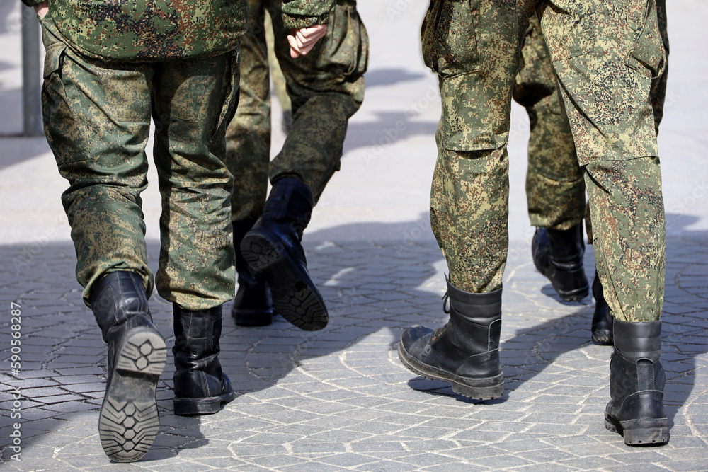 Legs of soldiers of military forces in camouflage, men in boots walking down the city street Legs of soldiers of military forces in camouflage, men in boots walking down the city street
