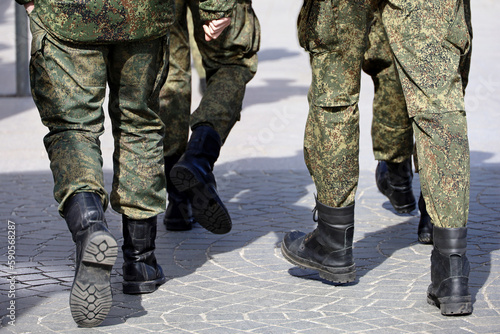 Legs of soldiers of military forces in camouflage, men in boots walking down the city street