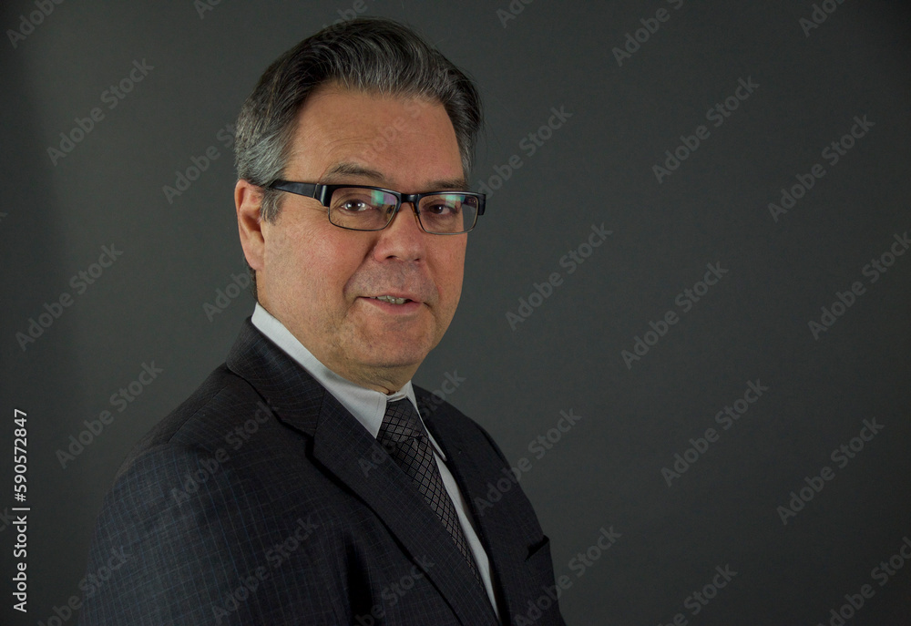 A man in a business suit looks and smiles at the camera with a gray background A man in a business suit looks and smiles at the camera with a gray background