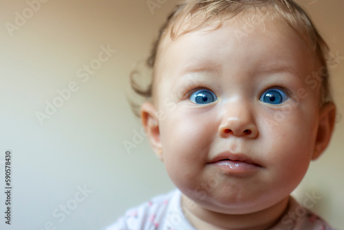 Blond baby girl face indicating surprise, wide open blue eyes with plump cheeks
