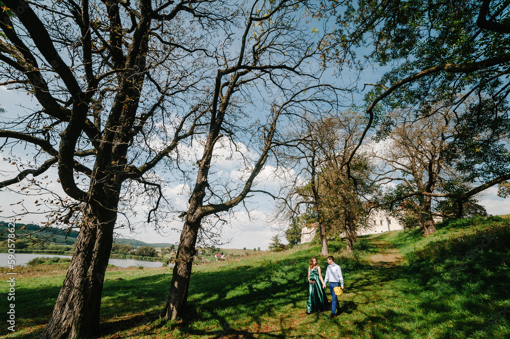 Happy pregnant couple walking in nature. Romantic moments pregnancy in park.