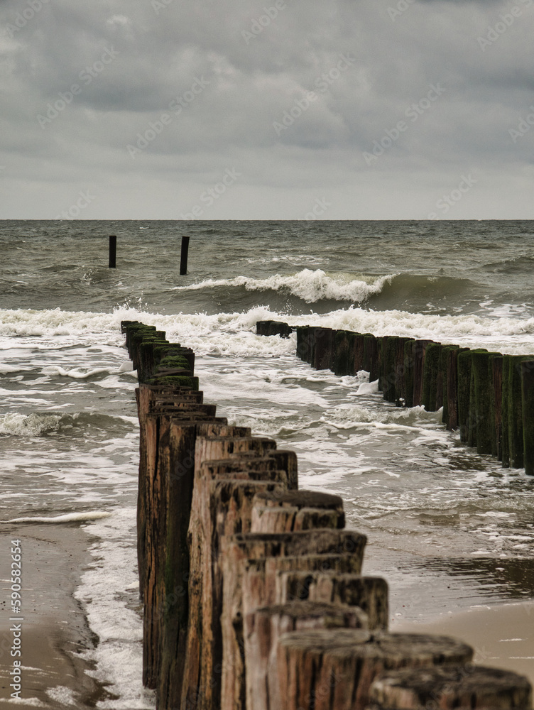 Holzpolder weisen den Blick in die stürmische Nordsee bei düsterem Wolkenwetter