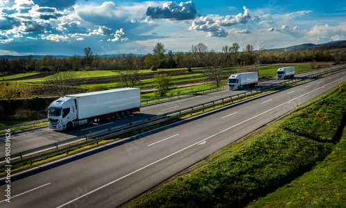 Fototapeta Naklejka Na Ścianę i Meble -  Highway transportation scene with three white transportation trucks in line on a rural highway under a beautiful blue sky