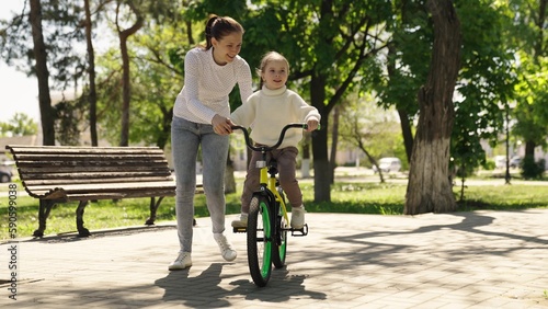 Happy family park. girl daughter rides bike for first time city park. mother teaches cheerful child girl ride bike. childhood dream travel. mother helps child girl ride bicycle by pedaling. traveling